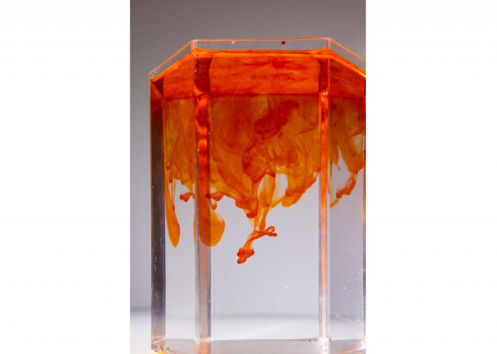 Glass jar filled with water showing orange food coloring diffusing throughout.