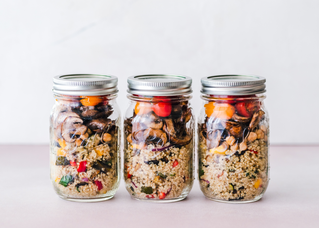 Row of three mason jars with canning lids on and filled with quinoa vegetable salad.