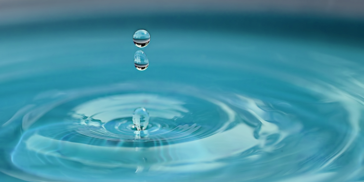 Close up of three drops of water falling into clear blue water.