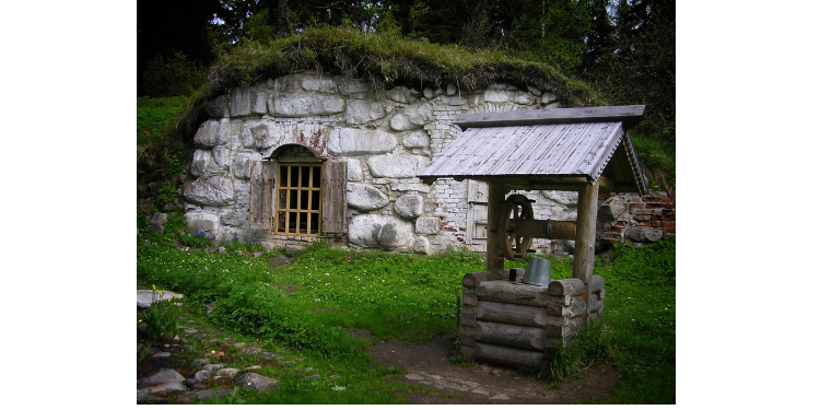 Stone cottage with grass top behind a small well house.