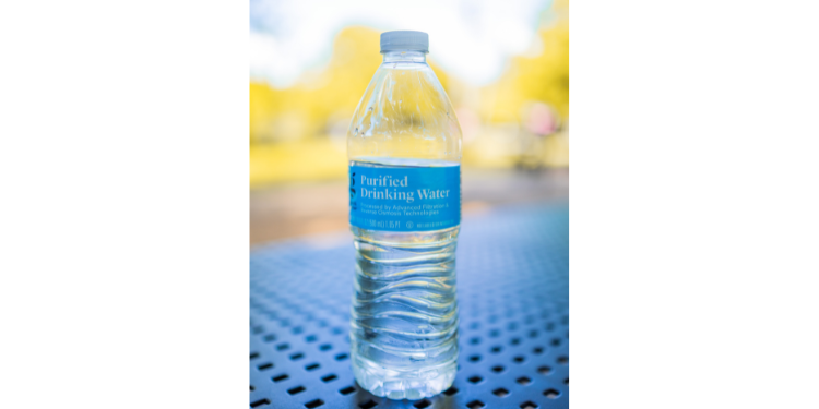 Plastic bottle of water sitting on metal table with purified drinking water label on bottle.