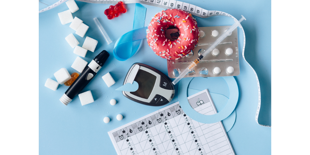 Sugar cubes, gummy bears, pink donut with sprinkles all on blue surface with blood sugar monitoring equipment and weight loss tools.