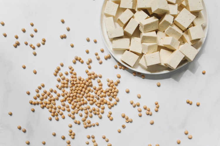 Bowl of tofu with scattered soybeans on the white table beside it.
