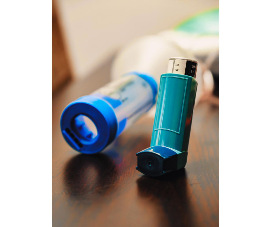 Asthma inhaler and spacer sitting on wooden table with more equipment in background.