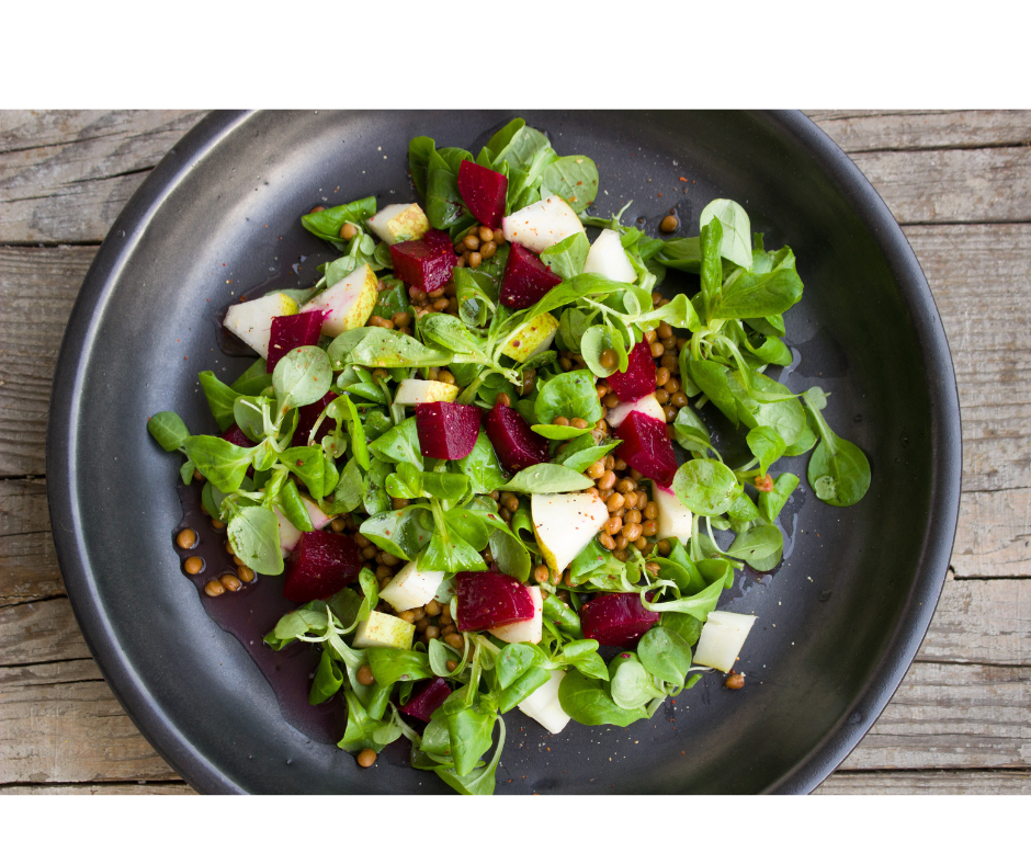 Salad greens with seeds and red beets chopped on top. In black bowl on wooden table.