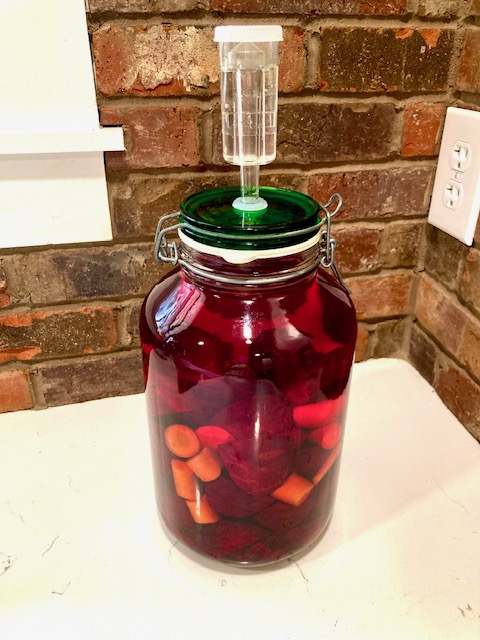 anaerobic fermenting jar with fermented beet kvass sitting on white counter with brick in background