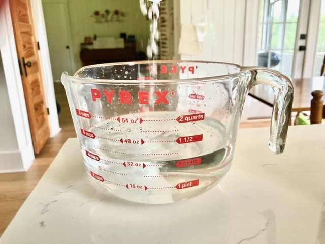 pyrex measuring container with water in it and salt falling into it sitting on counter