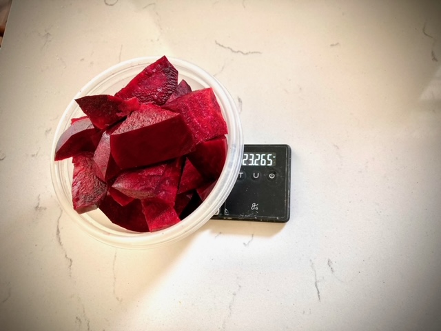 peeled and quartered beets in plastic container on small black scale sitting on white counter