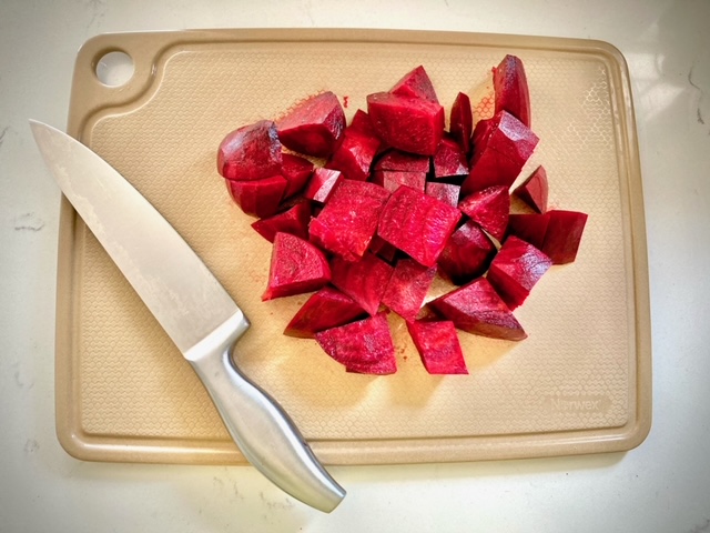 beets peeled and quartered in a pile on a brown cutting board with knife beside them all sitting on white counter